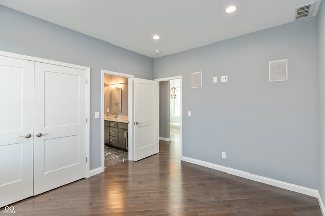 unfurnished bedroom featuring ensuite bathroom, a closet, dark wood-type flooring, and sink