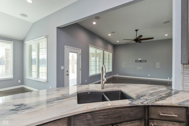 kitchen with light stone counters, vaulted ceiling, ceiling fan, sink, and hardwood / wood-style floors