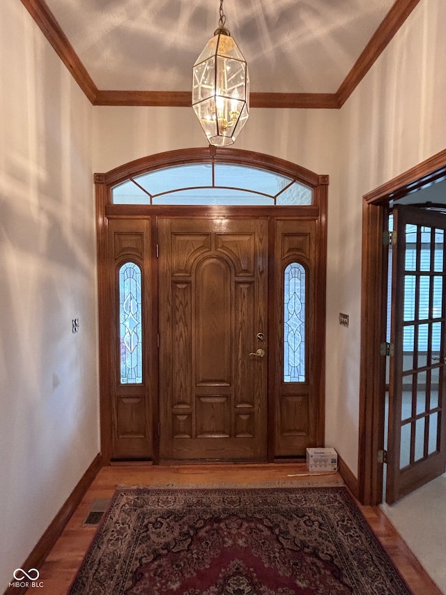 foyer entrance featuring ornamental molding, light wood-type flooring, and a notable chandelier