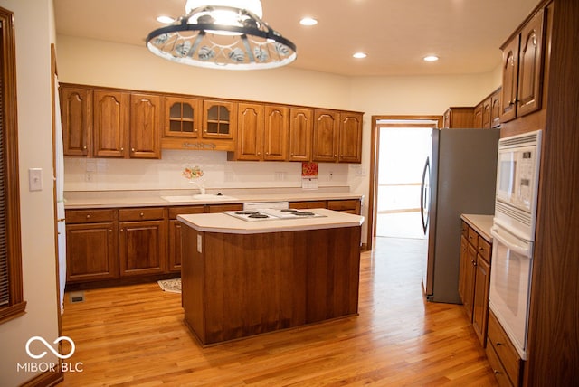 kitchen featuring a center island, white appliances, sink, hanging light fixtures, and light hardwood / wood-style floors