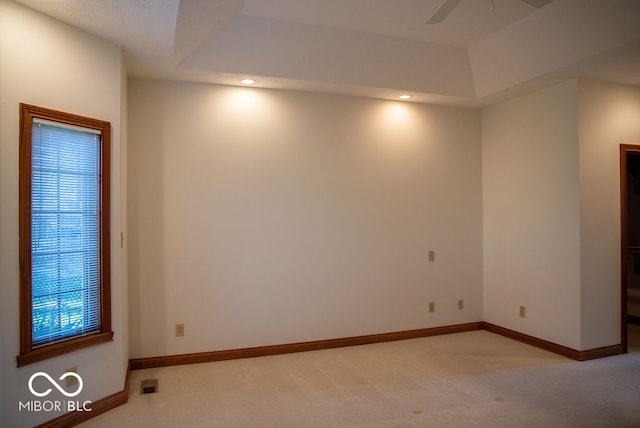 unfurnished room featuring a tray ceiling, ceiling fan, and light colored carpet