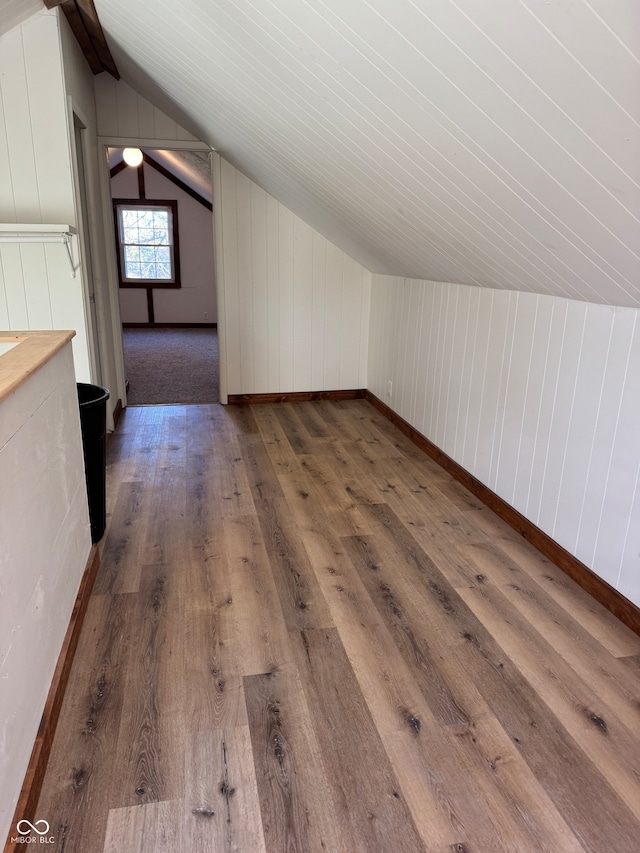 additional living space featuring dark hardwood / wood-style floors, vaulted ceiling, and wood walls