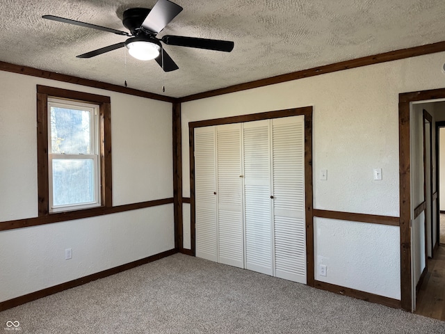 unfurnished bedroom featuring carpet flooring, ceiling fan, a textured ceiling, a closet, and ornamental molding