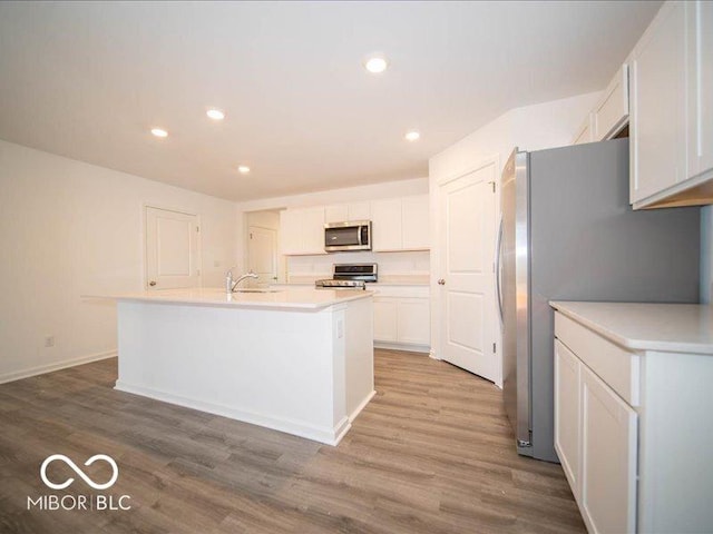 kitchen with white cabinets, appliances with stainless steel finishes, light hardwood / wood-style floors, and an island with sink