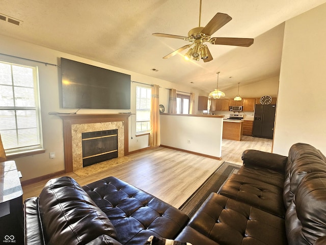 living room with ceiling fan, a textured ceiling, a premium fireplace, light hardwood / wood-style flooring, and vaulted ceiling