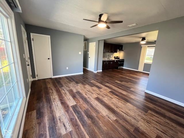 unfurnished living room with a textured ceiling, ceiling fan, sink, and dark wood-type flooring