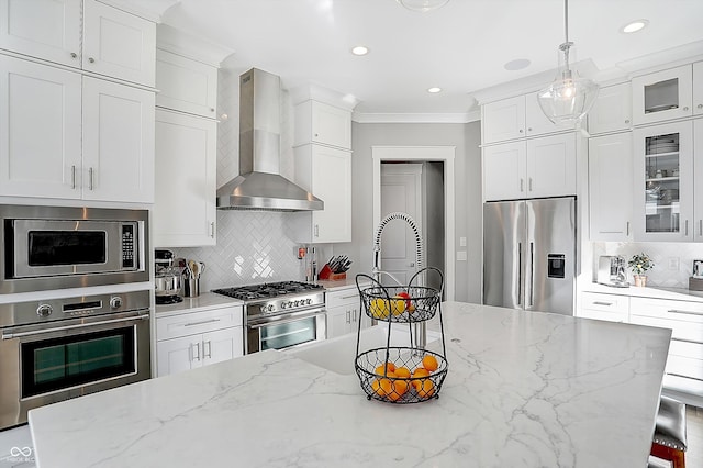 kitchen featuring pendant lighting, wall chimney exhaust hood, white cabinets, and appliances with stainless steel finishes