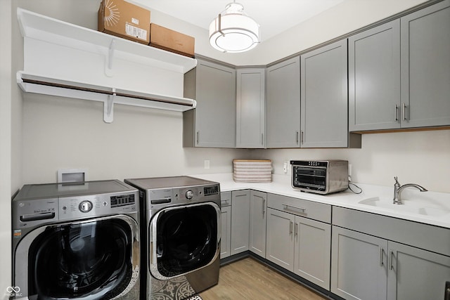 washroom with washing machine and clothes dryer, sink, cabinets, and light wood-type flooring