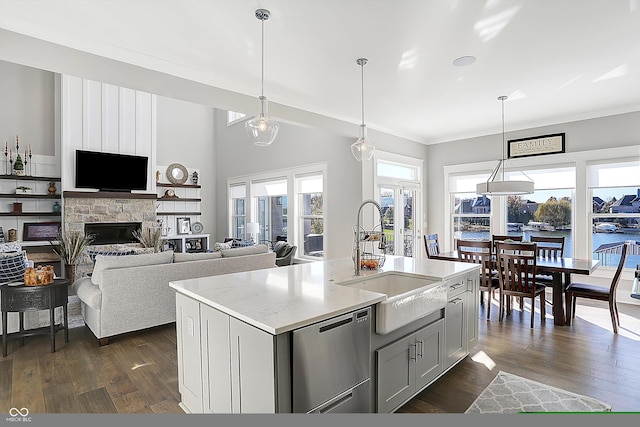 kitchen featuring a kitchen island with sink, sink, decorative light fixtures, dark hardwood / wood-style floors, and a stone fireplace