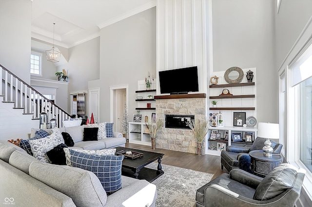 living room with a towering ceiling, crown molding, a notable chandelier, a fireplace, and hardwood / wood-style floors