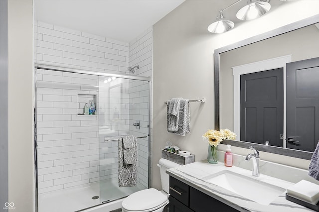 bathroom featuring a shower with door, vanity, and toilet