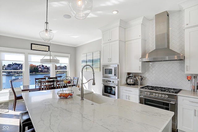 kitchen with appliances with stainless steel finishes, wall chimney range hood, pendant lighting, a water view, and white cabinets