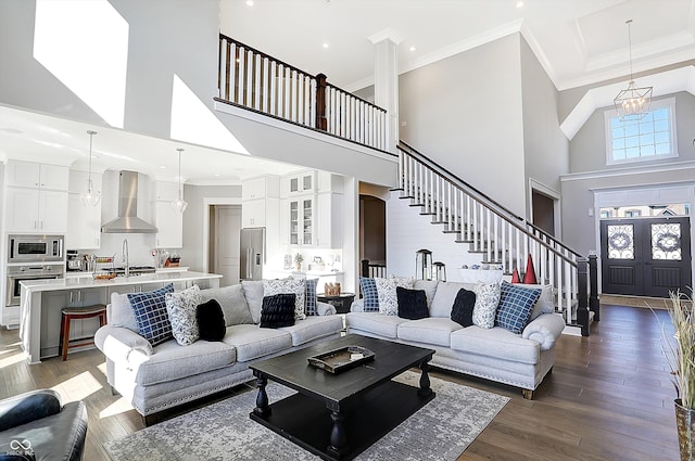 living room featuring crown molding, a towering ceiling, dark wood-type flooring, and an inviting chandelier