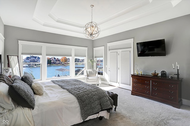 carpeted bedroom with a raised ceiling, a water view, and a chandelier