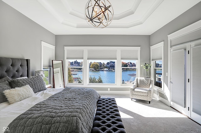 carpeted bedroom featuring a water view, crown molding, a tray ceiling, and an inviting chandelier