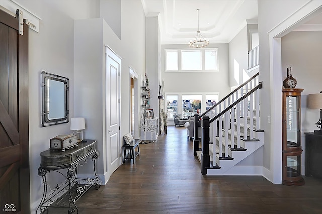 foyer entrance featuring a high ceiling, a barn door, dark hardwood / wood-style floors, a notable chandelier, and a tray ceiling