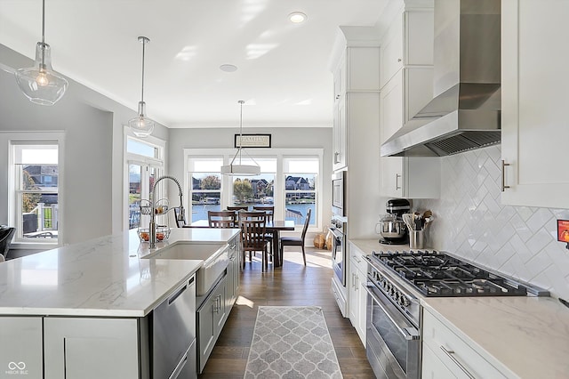 kitchen featuring appliances with stainless steel finishes, wall chimney range hood, an island with sink, and a wealth of natural light