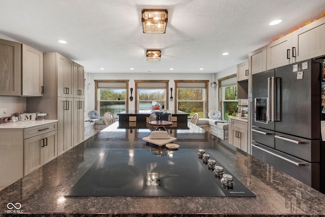 kitchen with dark stone countertops, black electric cooktop, a textured ceiling, and high quality fridge