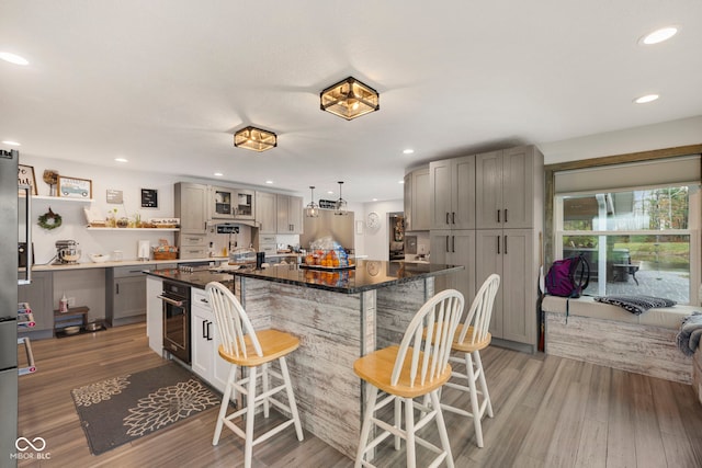 kitchen featuring gray cabinetry, a center island, a kitchen breakfast bar, hanging light fixtures, and light wood-type flooring