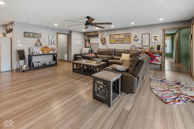 living room with ceiling fan, light hardwood / wood-style flooring, and a textured ceiling