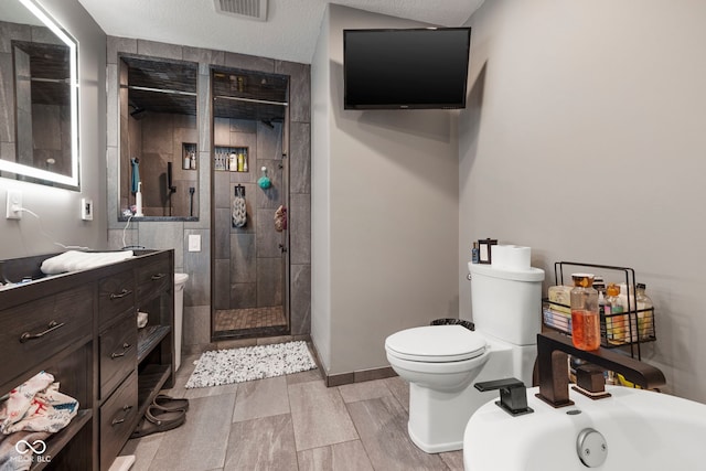 bathroom featuring vanity, a tile shower, a textured ceiling, and toilet