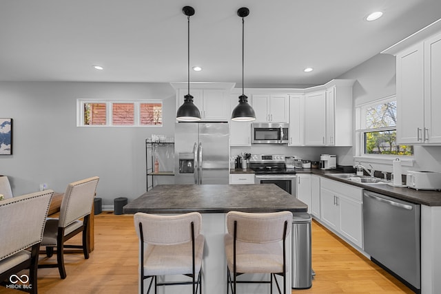 kitchen featuring light wood-type flooring, appliances with stainless steel finishes, decorative light fixtures, and white cabinets