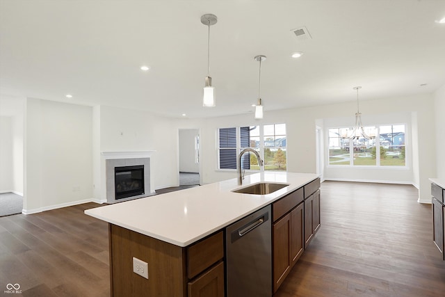 kitchen with a center island with sink, dark hardwood / wood-style floors, sink, stainless steel dishwasher, and a tile fireplace