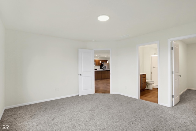 unfurnished bedroom featuring ensuite bathroom, carpet, and stainless steel fridge