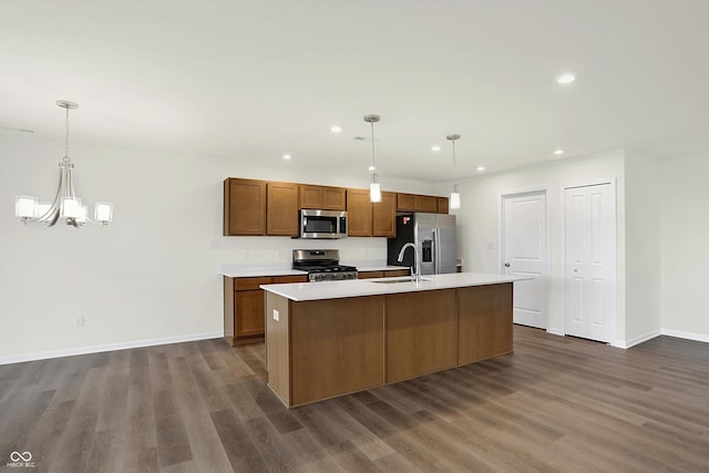 kitchen with appliances with stainless steel finishes, dark hardwood / wood-style flooring, pendant lighting, sink, and an island with sink