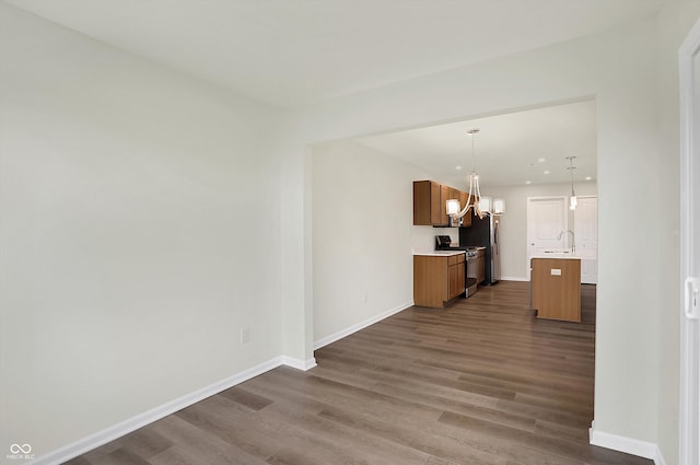 kitchen with dark wood-type flooring, sink, a kitchen island with sink, pendant lighting, and appliances with stainless steel finishes