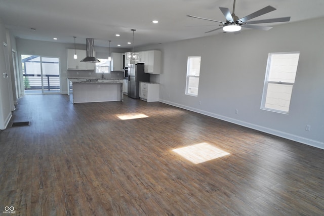 unfurnished living room with ceiling fan, a healthy amount of sunlight, and dark wood-type flooring