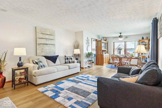 living area featuring light wood-type flooring, a textured ceiling, baseboards, and a ceiling fan