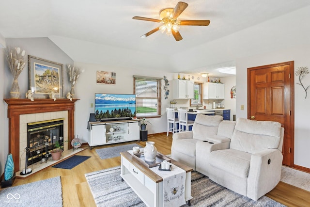 living room featuring light wood finished floors, a fireplace, ceiling fan, and vaulted ceiling