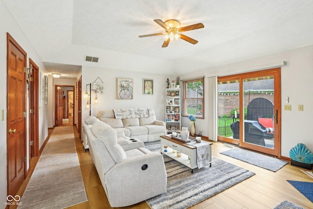 living area featuring a tray ceiling, a ceiling fan, visible vents, and wood finished floors