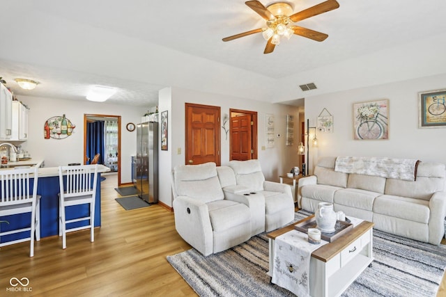 living area featuring light wood finished floors, visible vents, baseboards, and a ceiling fan