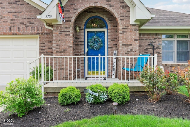 doorway to property with an attached garage, a shingled roof, and brick siding