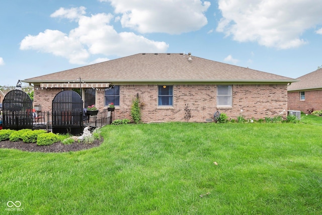 rear view of property featuring central air condition unit, roof with shingles, brick siding, and a lawn