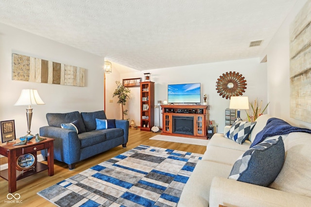 living area with a fireplace, a textured ceiling, visible vents, and wood finished floors