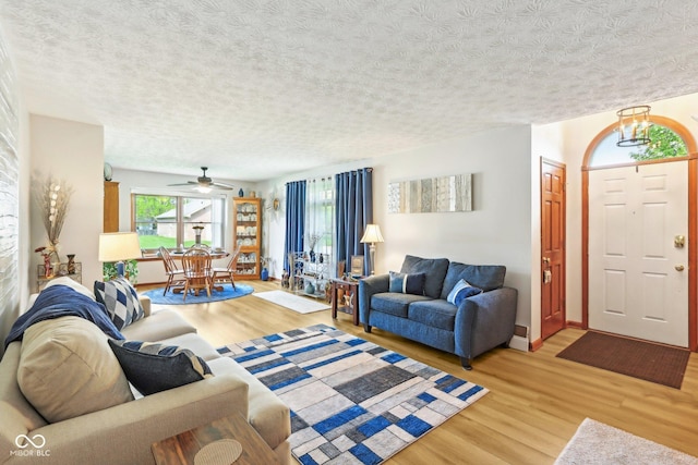 living area with light wood finished floors, a textured ceiling, baseboards, and a ceiling fan