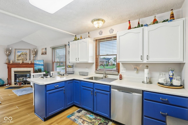 kitchen with a peninsula, a sink, white cabinetry, stainless steel dishwasher, and blue cabinets