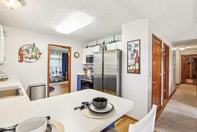 kitchen with light wood-type flooring, a textured ceiling, white cabinetry, light countertops, and appliances with stainless steel finishes