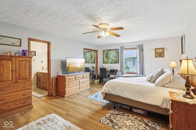 bedroom with a ceiling fan, ensuite bathroom, light wood-type flooring, and a textured ceiling