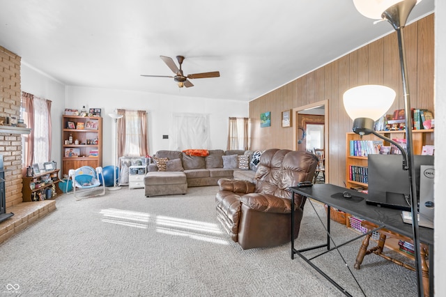 living room featuring a brick fireplace, wood walls, ceiling fan, and carpet floors