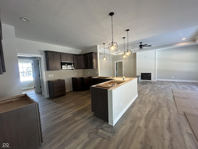 kitchen featuring a fireplace, wood-type flooring, hanging light fixtures, ceiling fan, and dark brown cabinets