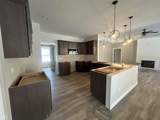 kitchen with a large fireplace, dark brown cabinetry, decorative light fixtures, and hardwood / wood-style floors