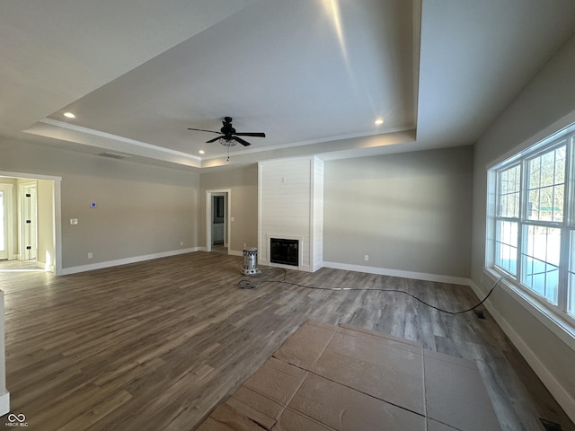 unfurnished living room featuring a fireplace, hardwood / wood-style flooring, ceiling fan, a raised ceiling, and crown molding