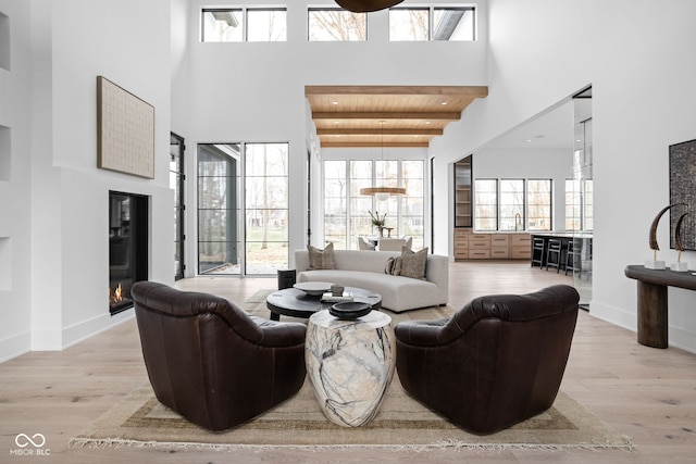 living room with beam ceiling, wooden ceiling, a high ceiling, and light hardwood / wood-style flooring