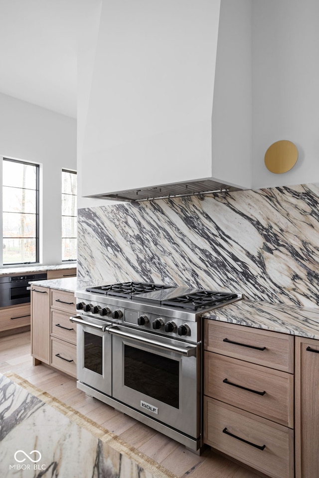 kitchen with backsplash, light brown cabinetry, double oven range, and light hardwood / wood-style flooring