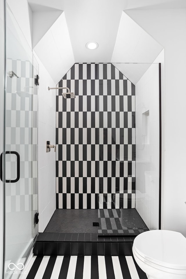 bathroom featuring a tile shower, toilet, and lofted ceiling