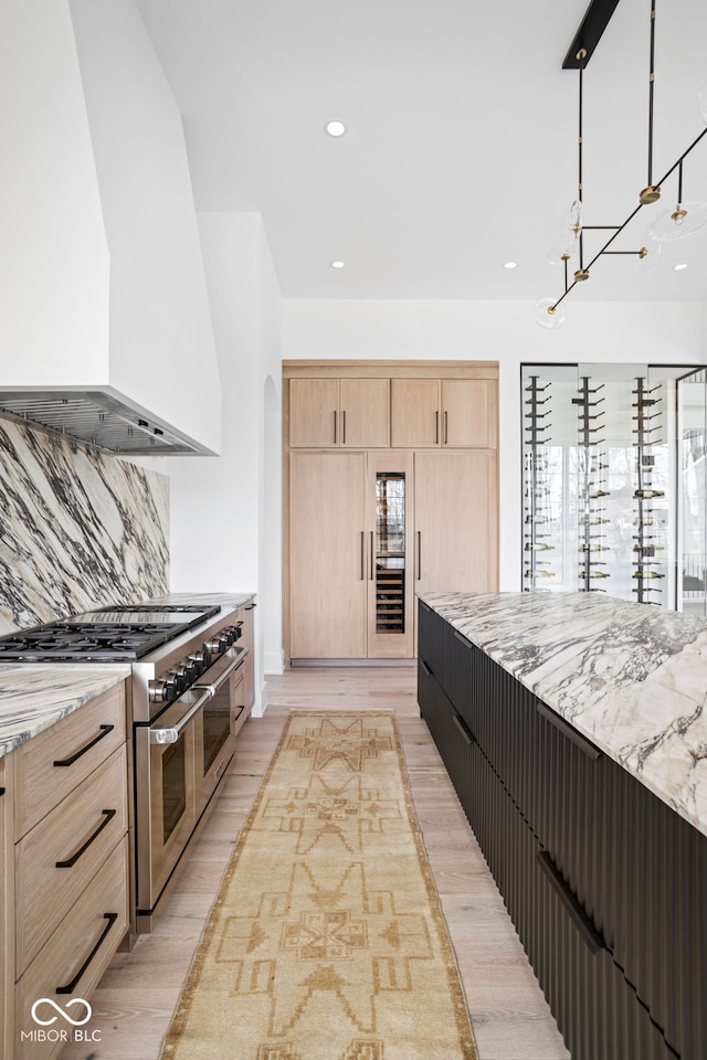 kitchen featuring custom exhaust hood, double oven range, light hardwood / wood-style flooring, light stone countertops, and light brown cabinetry